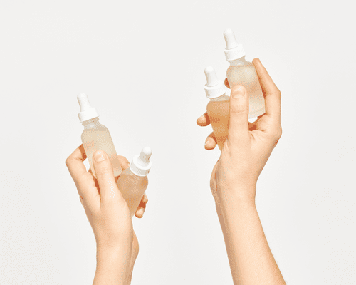 Two hands holding two glass serum bottles each