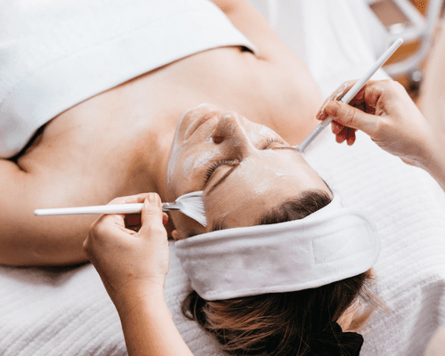 A woman in a towel laying on a treatment table receiving a facial 