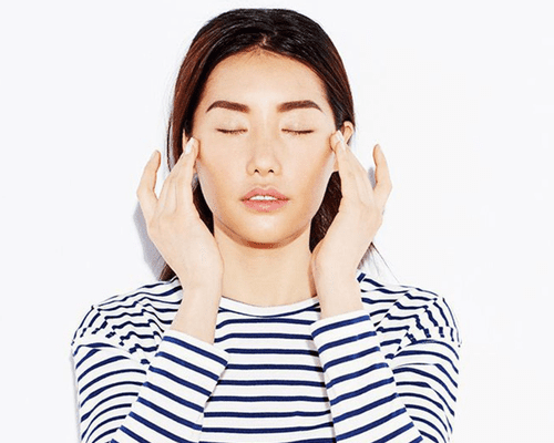 A woman in a striped shirt using her hands to give herself a facial massage