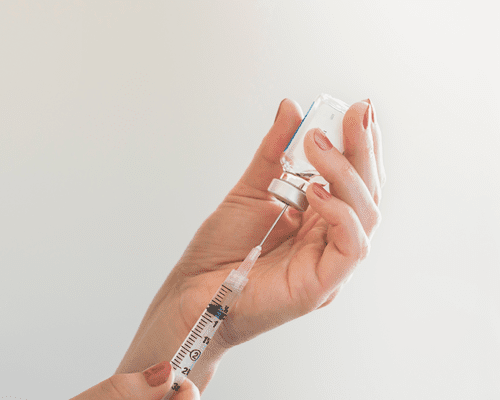 A hand holding a vial and another hand holding a syringe