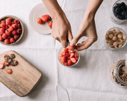 Close up of hands cutting strawberries, blueberries, bananas and oats