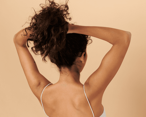 A woman from the back with her arms up, putting her hair into a ponytail