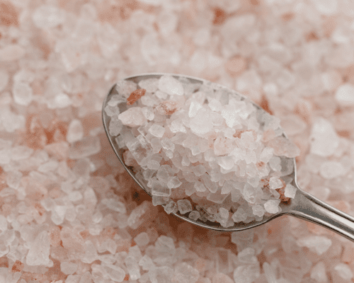 Pink Himalayan salt on a silver spoon, with a background of pink salt. 