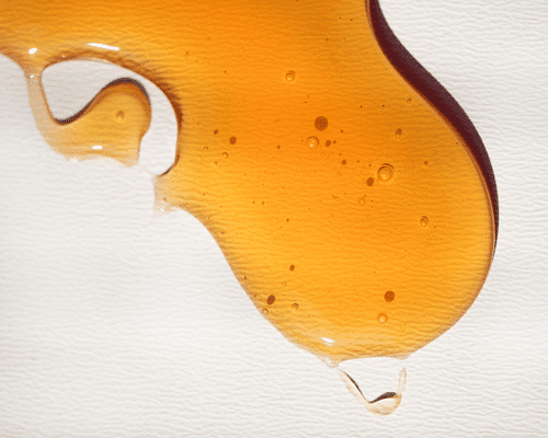 A circular, elongated drop of honey on a textured white background.