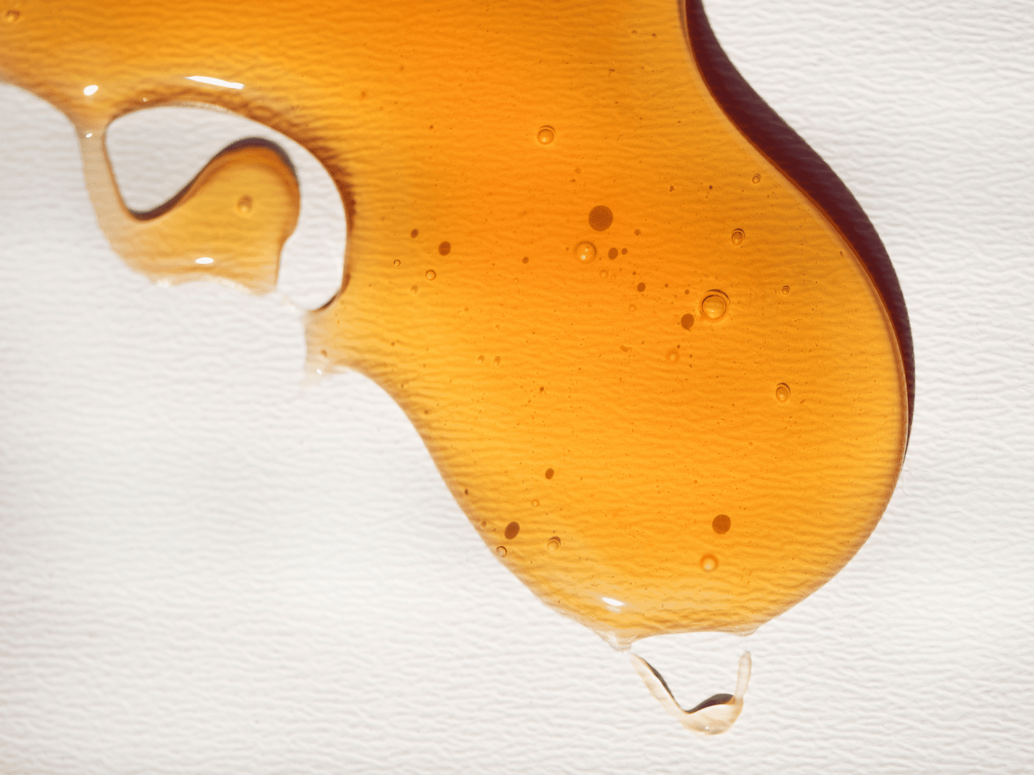 A circular, elongated drop of honey on a textured white background.