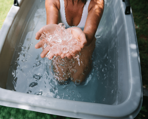 A woman from the neck down in a bathing suit, holding ice in her hands in an ice bath