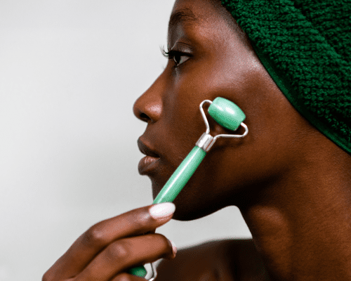 woman using a jade roller on cheek