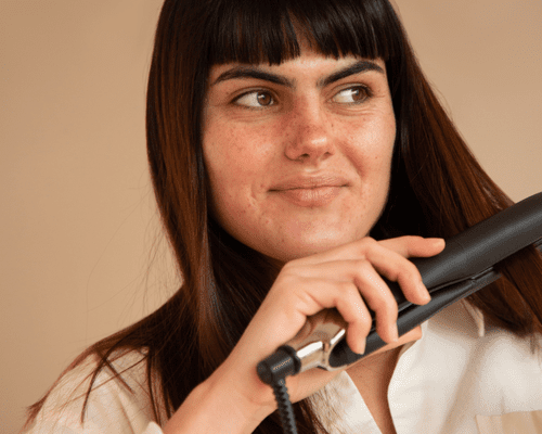 A woman with bangs and straight hair running a hair straightener through her hair