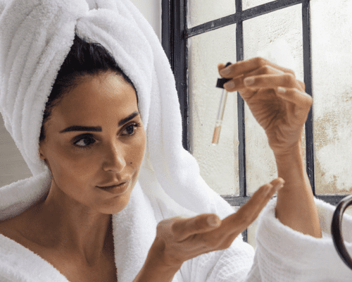 A woman in a bathrobe and her hair in a towel dropping oil from a dropper into her hand