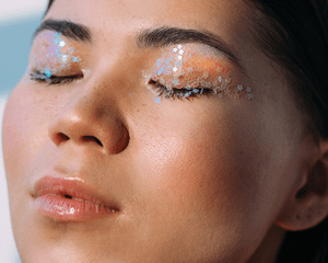 A woman with glossy lips and her eyes closed with star sequins on the lids