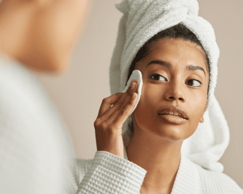 Close up of a woman in a robe cleansing her face with a wipe