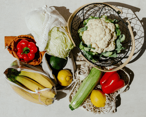 Assorted fruits and vegetables in white mesh bags on a white background. 