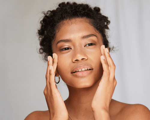 A close up of a curly haired model holding the temples of her face.