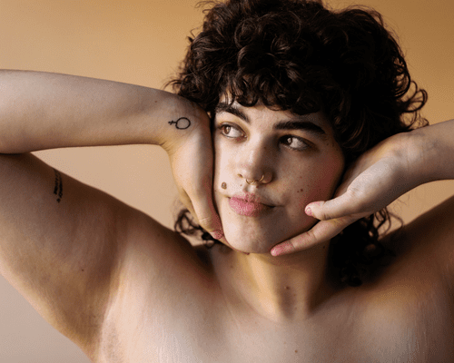 Close up of a brown curly-haired woman with two arm tattoos.