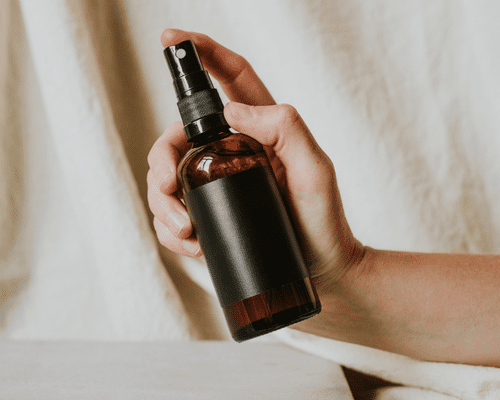 A hand holding a spray bottle on a neutral background