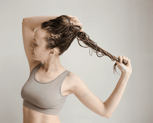 A woman in a sports bra holding her wet hair and pulling at the end