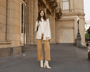 A woman styled in a white shirt and booties with mustard-colored pants