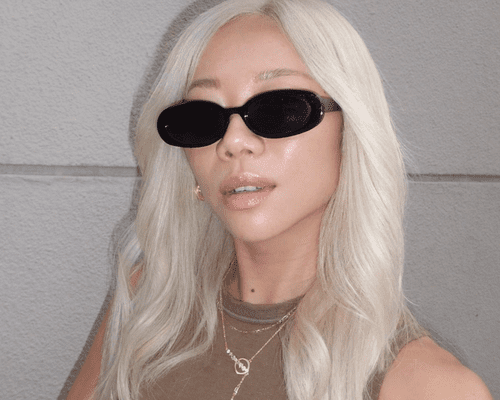 Former Editorial Director of Byrdie Faith Xue wearing black round sunglasses and medium length platinum blonde hair. 