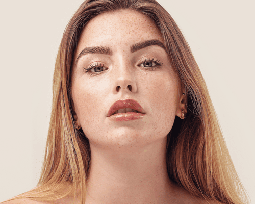 Close-up of woman with freckles, full eyebrows, and plump lips.