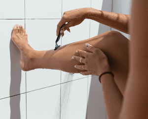 A close up of a model shaving their shin hair with a razor. 