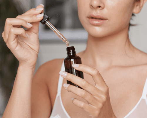 A woman holding a serum bottle and dropper in her hands