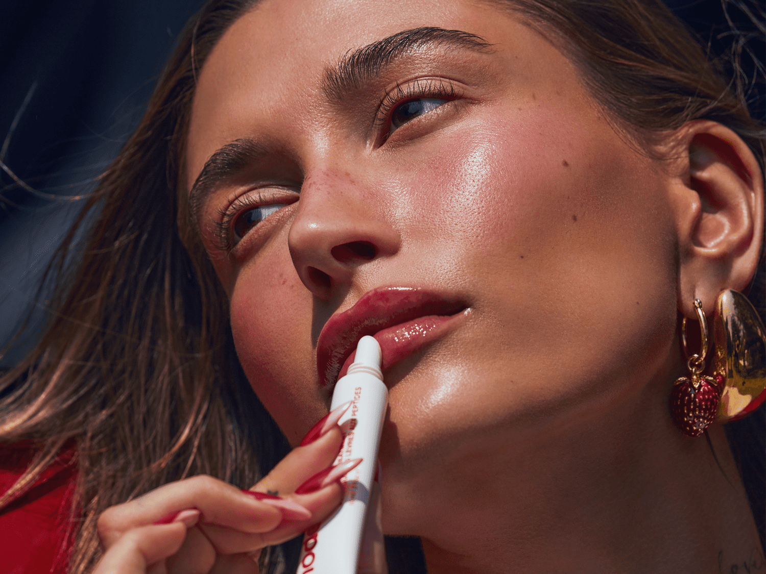 Hailey Bieber applying the new Rhode Strawberry Glaze Peptide Lip Treatment