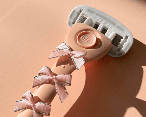 close up of pink razor with bows on pink background