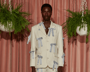 Model wearing white suit with powder blue bow appliques while standing near hanging plant baskets