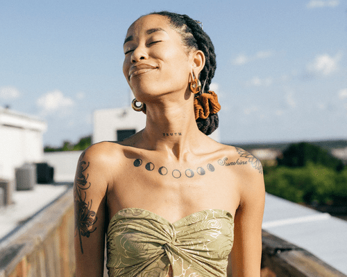 Woman with locs with her eyes closed while taking in the sunshine at a rooftop party.