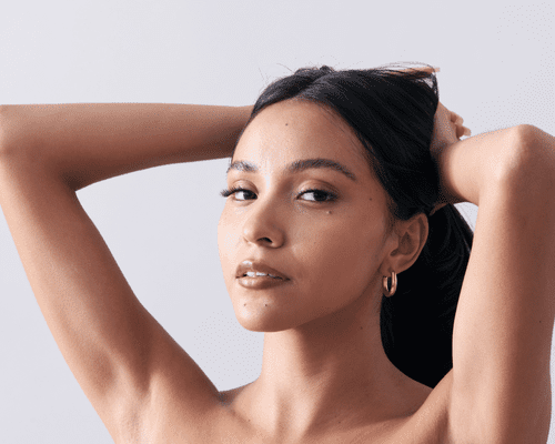 A young Latina woman lifts thick hair up from face and looks at camera.