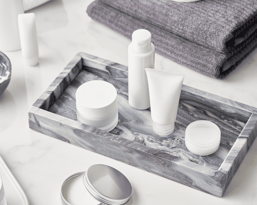 A marble tray with white, unlabeled moisturizer tubes, jars and bottles on it