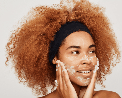 Close up of a black woman with curly red hair washing face.