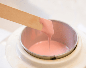 Image of a stick with pink wax being warmed in a warmer