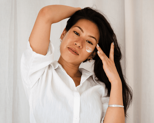 woman with swatch of moisturizer on cheek against white background