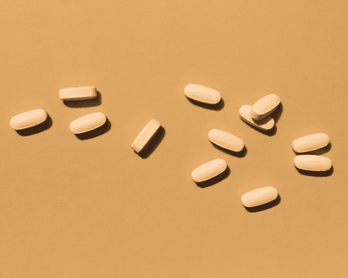 A close up of light yellow pill tablets on a warm burnt orange background. 